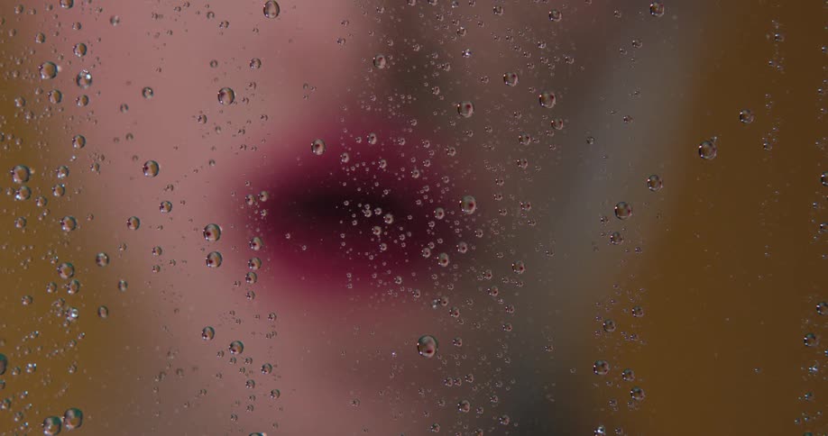 A person smoking a cigarette with a glass window with water droplets in the foreground