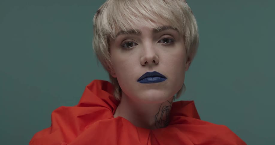 A blonde female model with blue lips and wearing an orange top
