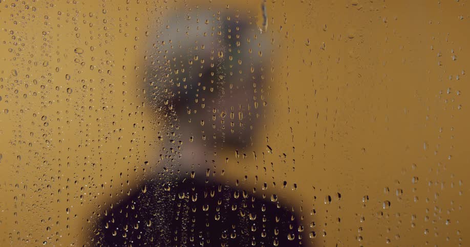 A man out of focus with a glass wall with droplets in front of him