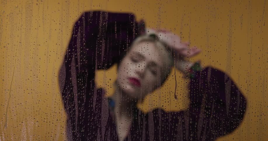 A woman is standing near a window when its raining