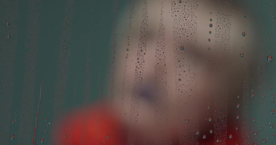 A woman with short hair poses behind a glass pane covered in drops of water