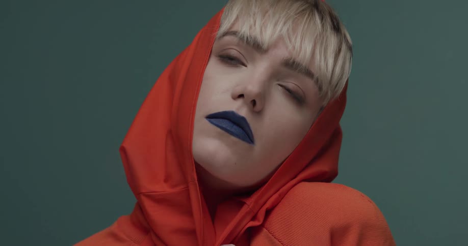 A blonde model with blue lips and an orange hood poses for the camera