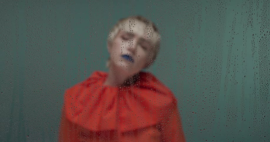 Young blonde short haired woman modeling behind a wet glass pane