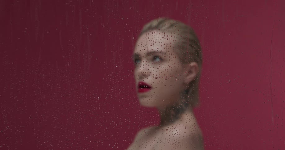 Woman with red lipstick behind a glass with water droplets in front of a red wall