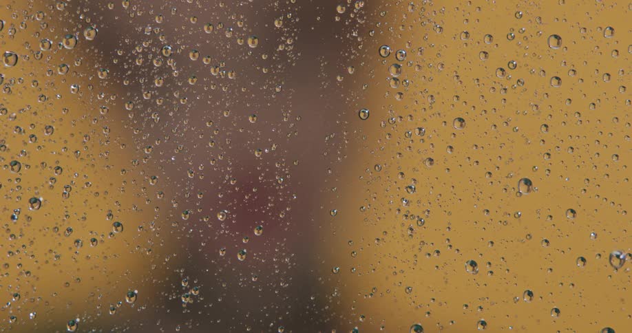 A blurry yellow background with a piece of glass with water droplets