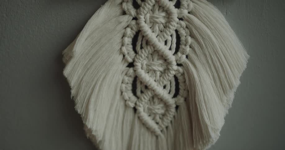 A wall decoration made of thick woven strands of yarn hangs from a wooden stick