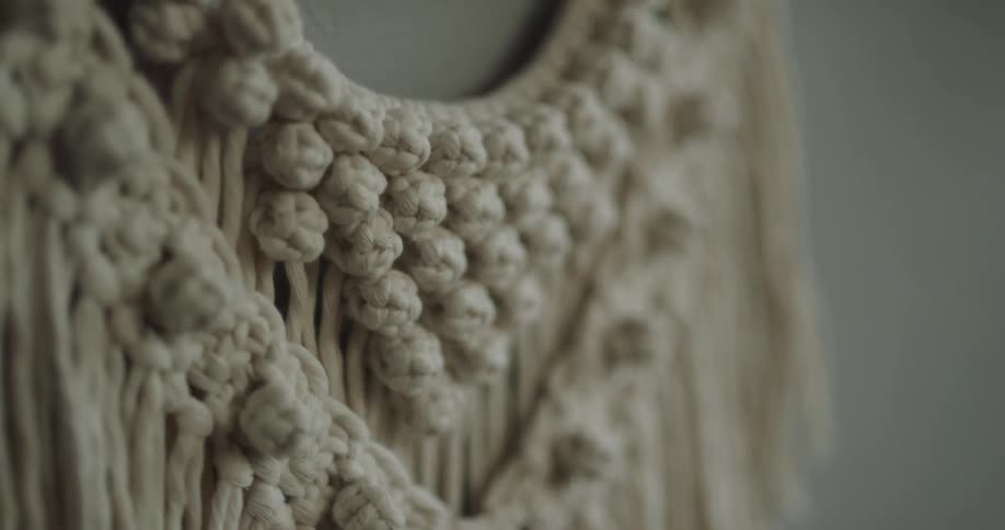 A craft made out of thick strands of knitted yarn hangs indoors on a wall