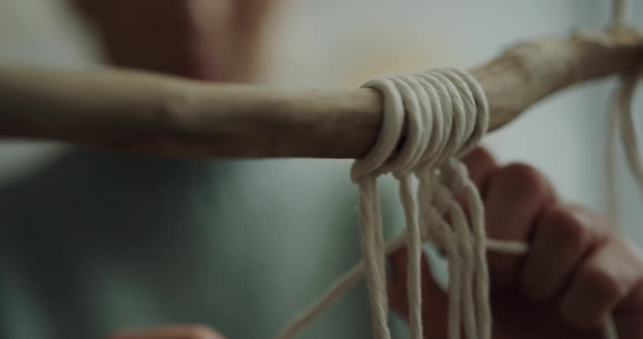 Young woman braiding decorations using string and dry tree branches