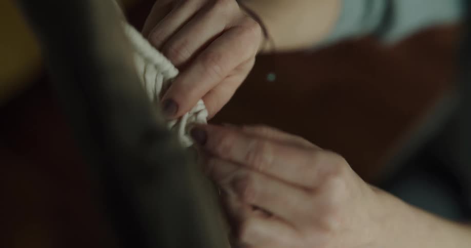 A woman in a room weaving string into fabric with her hands