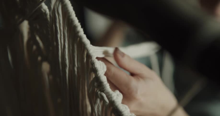 A woman uses her hands to macrame with white rope