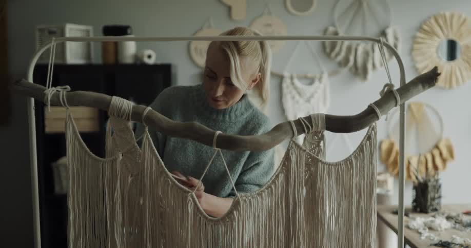 A woman in a sweater uses thick skins to weave an artwork
