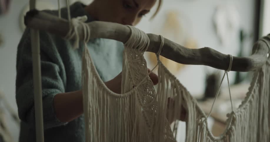 A woman in a room weaving string into fabric with her hands