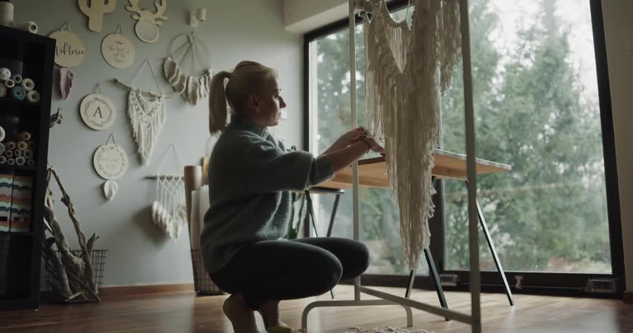 Woman trims macrame hanging on a rack indoors