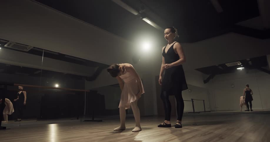 A young girl shows frustration while working on a ballet move with her teacher