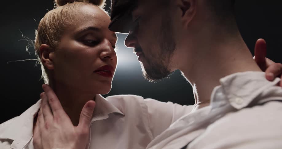 A man and woman dance closely together in a dark room with single spotlight