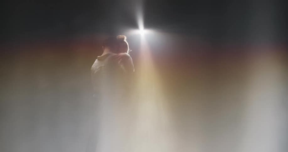 Dance partners move their hips in unison as they dance in front of a bright light in a hazy room