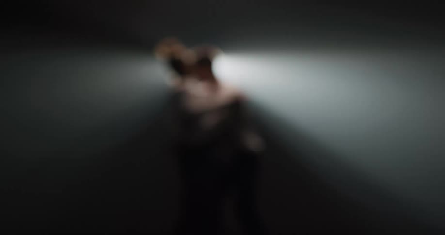 Silhouette of a couple dancing tango in front of a spotlight on a dark room
