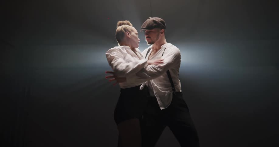 A man and woman dance together in a dark room with a light shining on them from behind