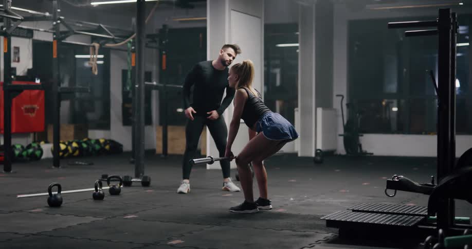 A man coaching a woman while she lifts weights in a gym