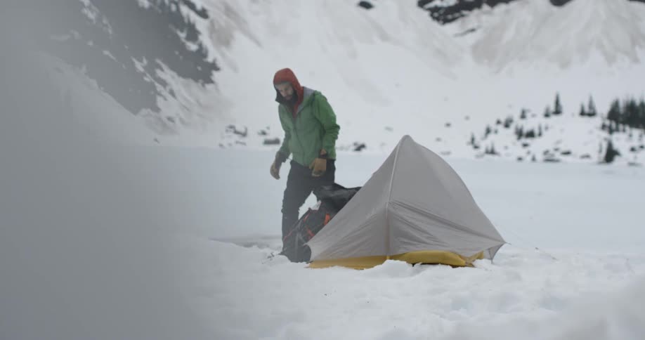 A man is walking over to a tent in the snow
