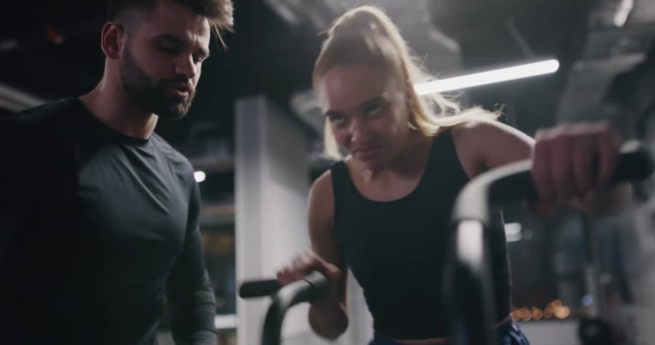 Coach training a woman on an elliptical cross trainer machine in a gym