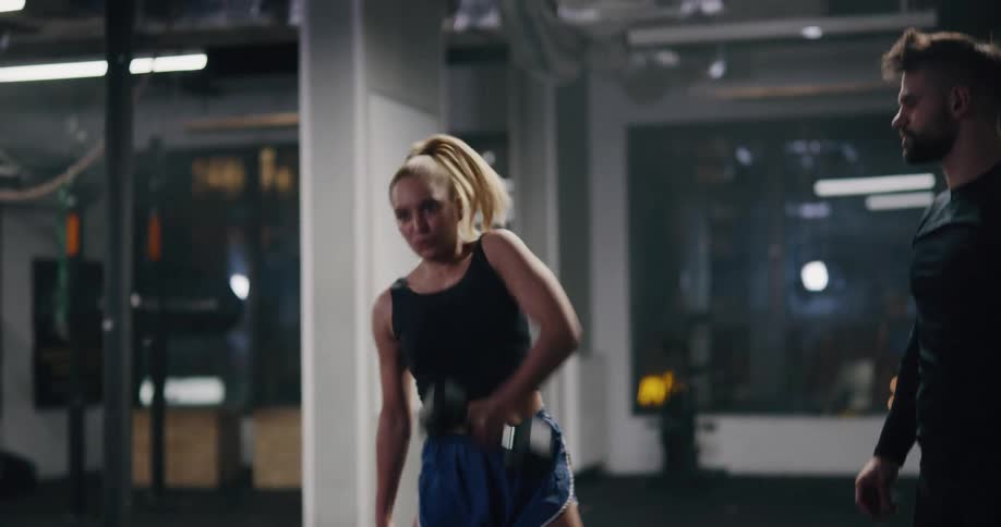 Young fit blonde woman training with dumbbells in a gym
