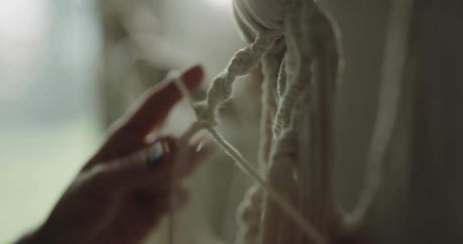A person is stringing yarn indoors during the day