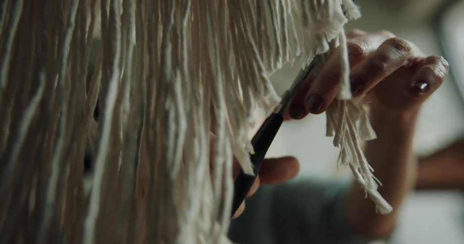 A woman uses a pair of scissors to trim and shape a row of hanging yarn