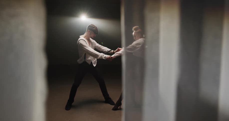 A man and a woman in a room dancing with a curtain in the foreground and a wall and a light in the background