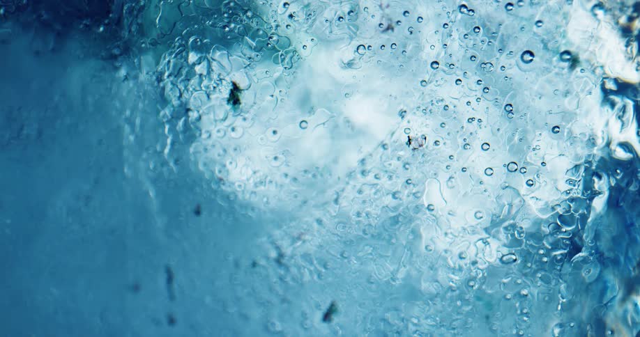 Sunlight shines through clear blue ice and causes droplets to melt