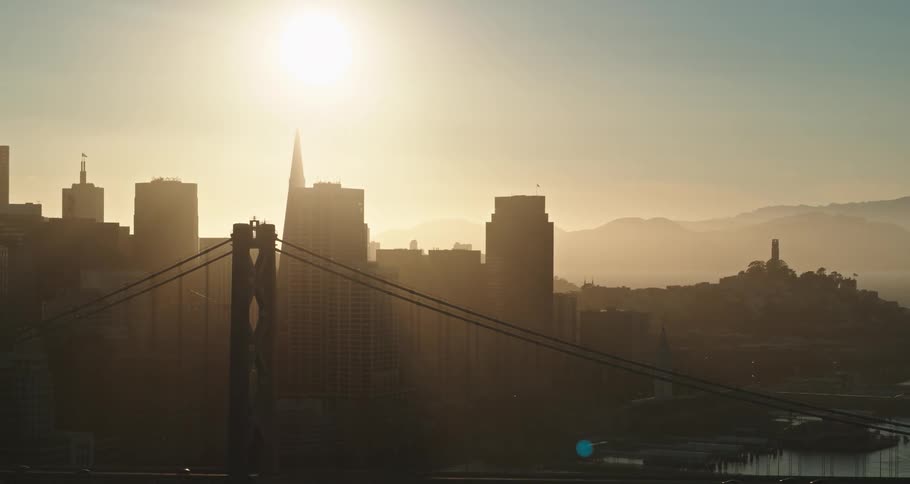 An aerial view of a city skyline and cars driving over a suspension bridge