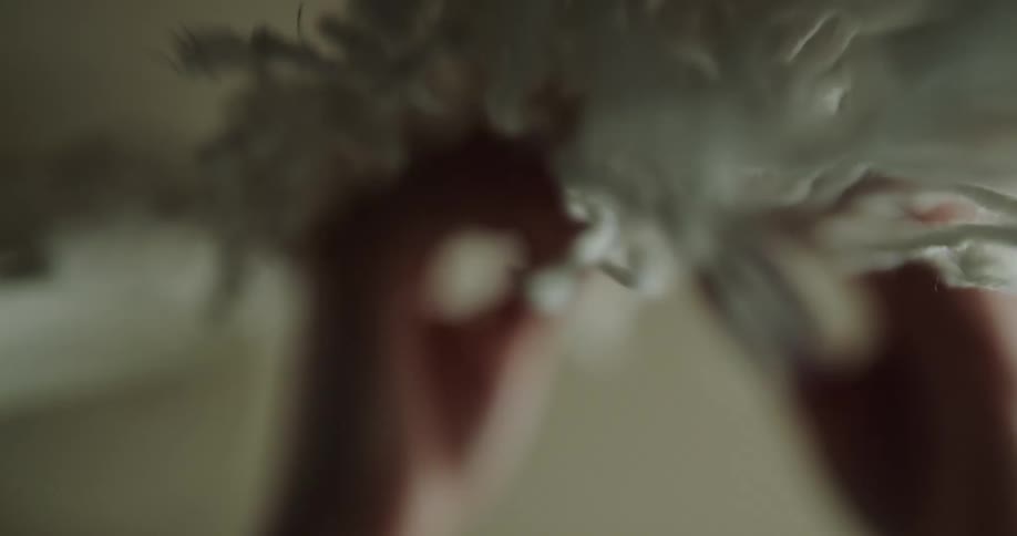A person strokes a hanging bundle of yarns indoors