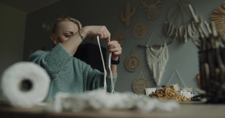A woman sitting in a room unraveling and cutting a string with a wall in the background