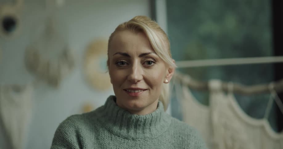 A blonde woman wearing a turtleneck sweater and earring smiles at the camera