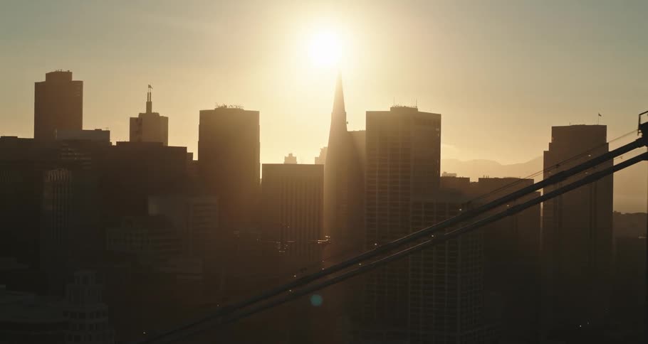 A skyline with buildings a bridge mountain and a bright sun