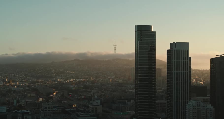 Cloud hangs over foggy mountains bordering city as traffic snakes along streets passing skyscrapers