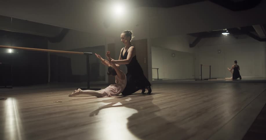Ballet instructor teaching a young girl how to stretch and pose in a studio