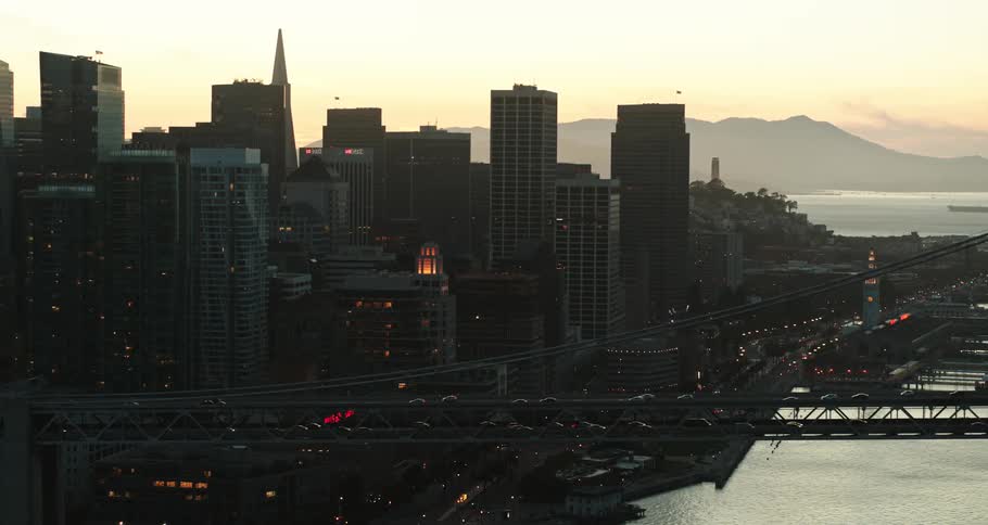 A skyline with a city and traffic with a bridge over water and mountains in the background
