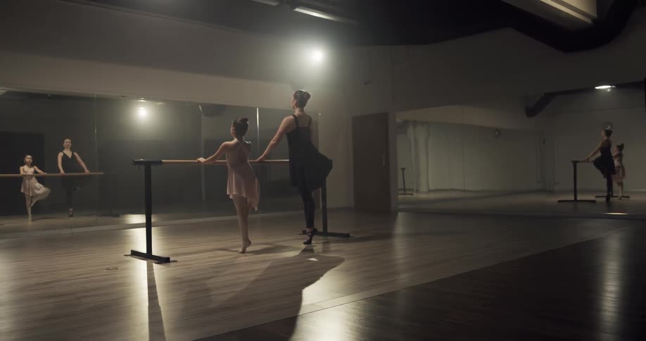 A ballet teacher corrects her student at the barre as their image is reflected in the mirrors around them