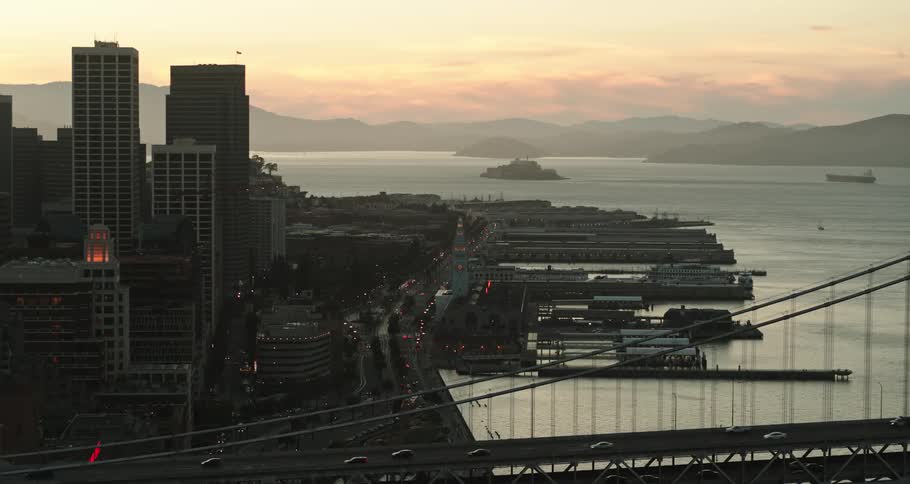 A bridge with vehicles with buildings a body of water the sky and clouds in the background