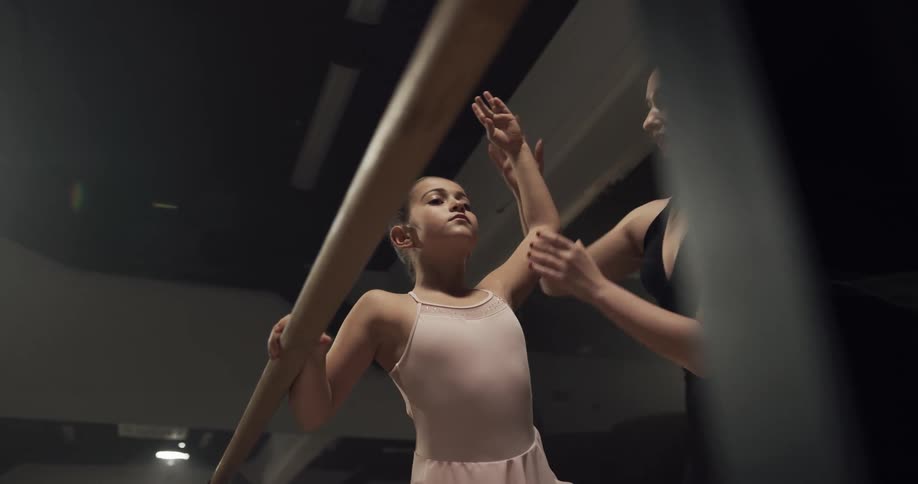 Ballet instructor teaching a young girl how to hold a pose in a studio