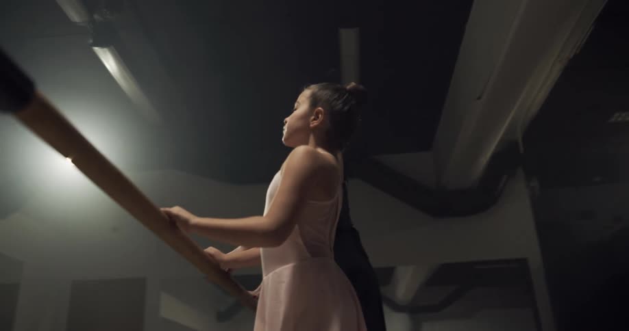 A girl trains at the ballet barre beside her teacher in a dance studio
