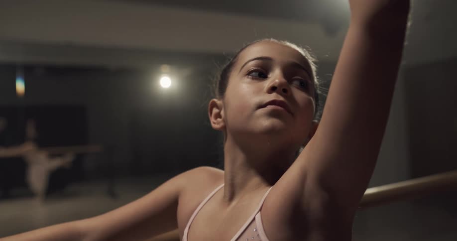 A little girl is in a ballet pose at a barre