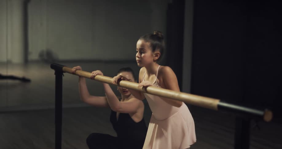 A woman and a girl in a dance studio stretching and holding on to a ballet bar