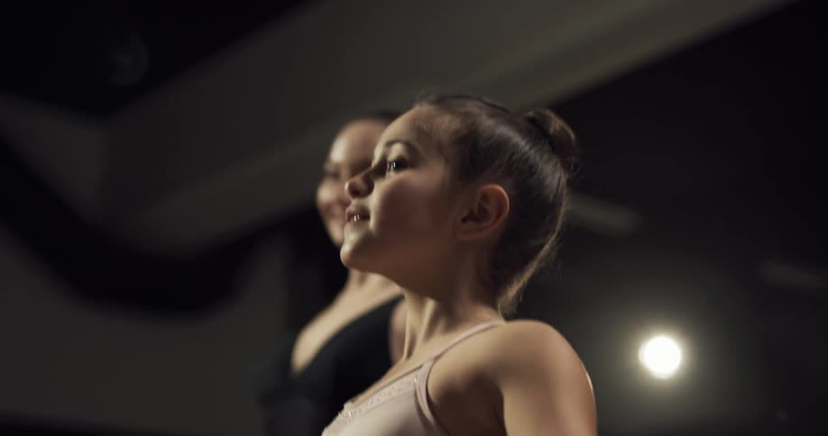 A girl practices ballet movements alongside an older woman in a ballet studio