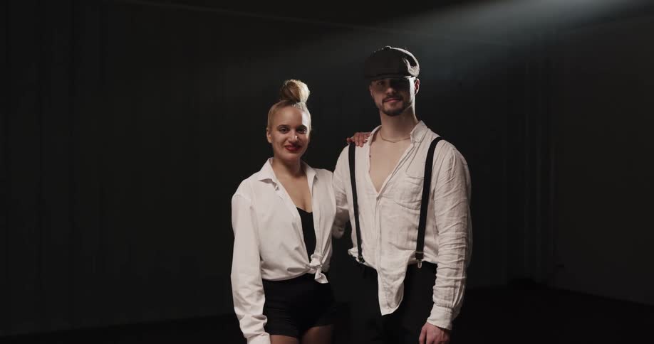 A man and woman stand on a stage with a spotlight smiling at a camera