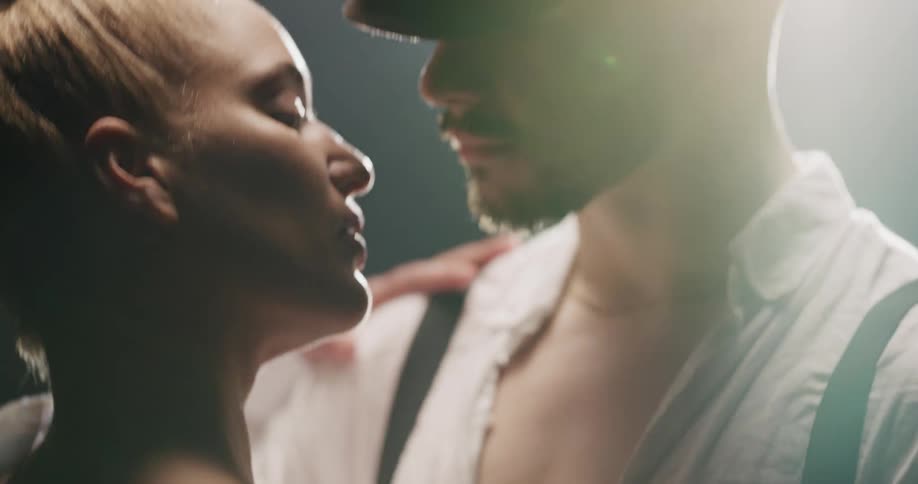 A man and woman dance intimately under a light in a dark room