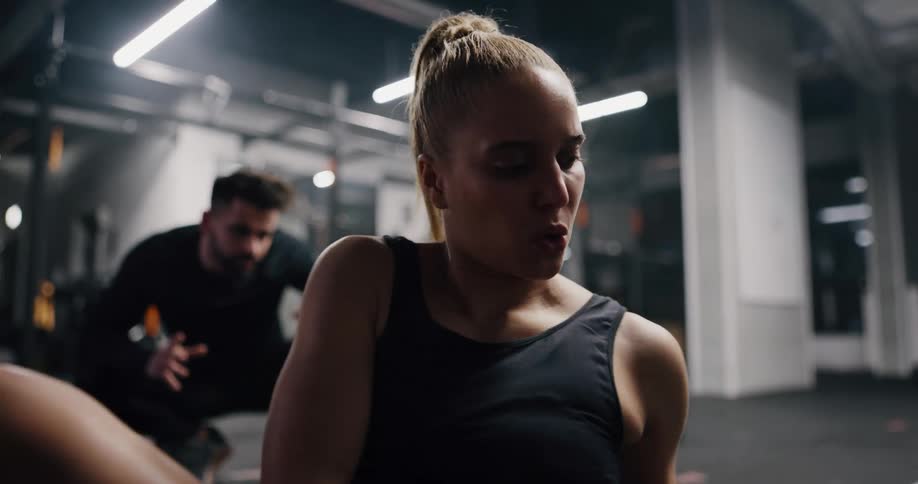 A woman trains in a gym with a weight as her trainer encourages her