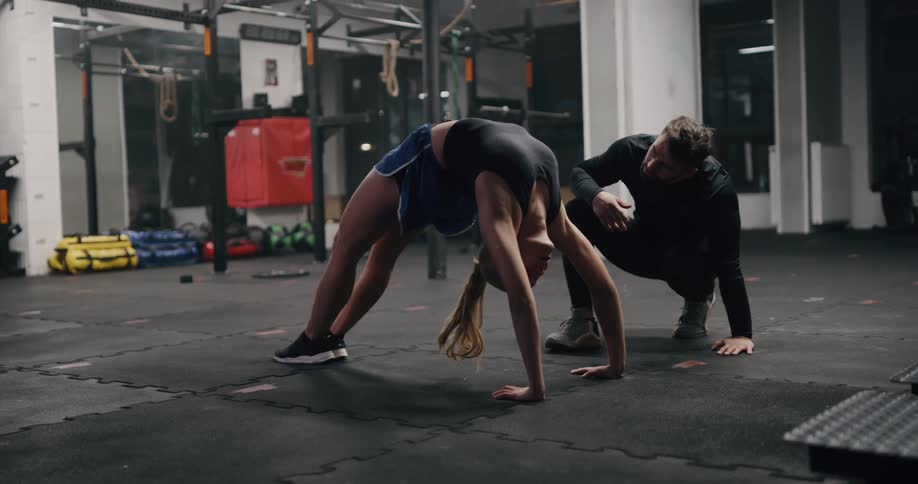 A woman does a back bend stretching in a gym with a trainer
