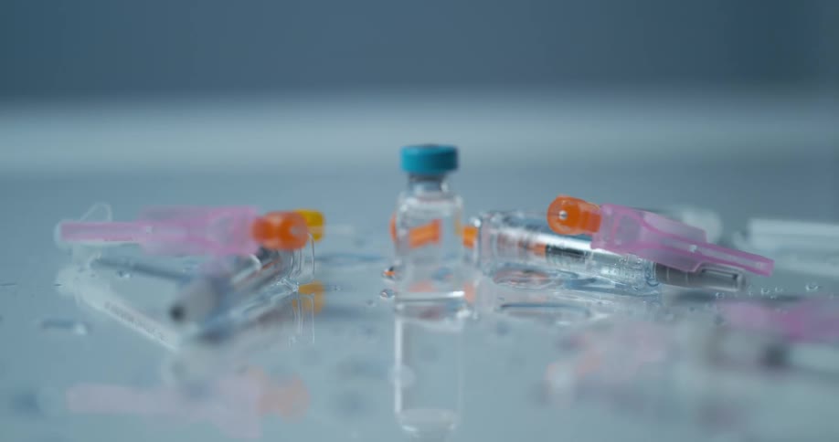 A wet surface containing a bottle and a group of syringes suddenly jolts sending the water and objects tumbling into the air